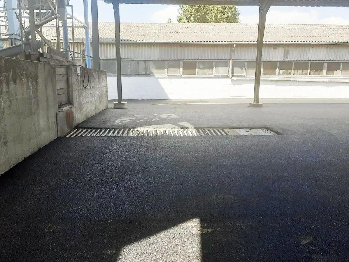 Aszfaltozott udvar vízelvezető folyókával ipari csarnok mellett