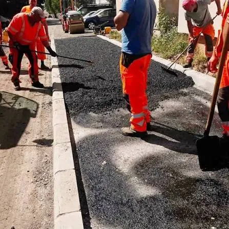 Munkások gereblyével és lapáttal terítik a meleg aszfaltot a szegélykő mellett