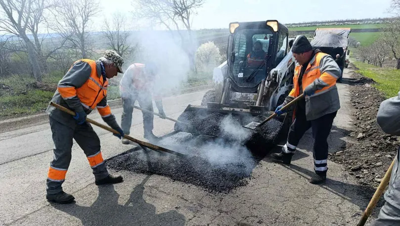Munkások Bobcat rakodó kanalából lapátolják a gőzölgő meleg aszfaltot a kátyúba